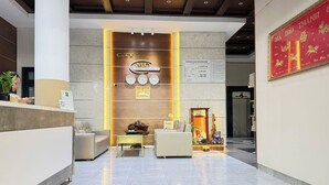 A modern hotel lobby with a reception desk, seating area, and a decorative wall with a clock and framed pictures. - Doi Ngoai Bien Phong SPA Hotel (Buon Ma Thuot)