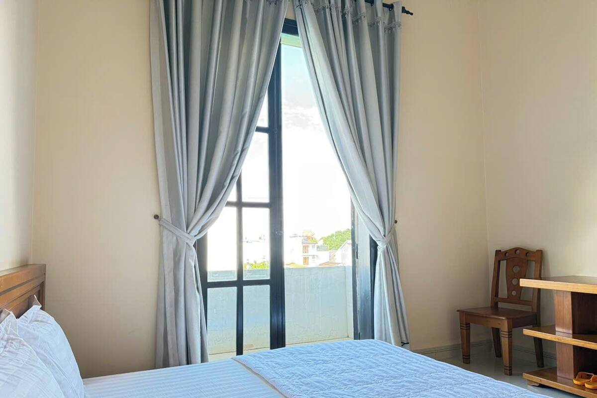 A hotel room with a bed, a desk, and a chair. There is a window with curtains.