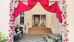A hotel entrance with a large red bow, steps leading to the lobby, and a motorcycle parked outside. - Doi Ngoai Bien Phong SPA Hotel (Buon Ma Thuot)