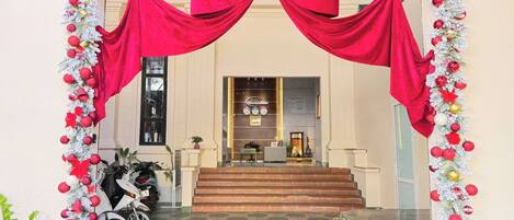 L’entrée d’un hôtel, ornée d’un grand nœud rouge, avec des marches menant au hall d’accueil et une moto garée à l’extérieur.