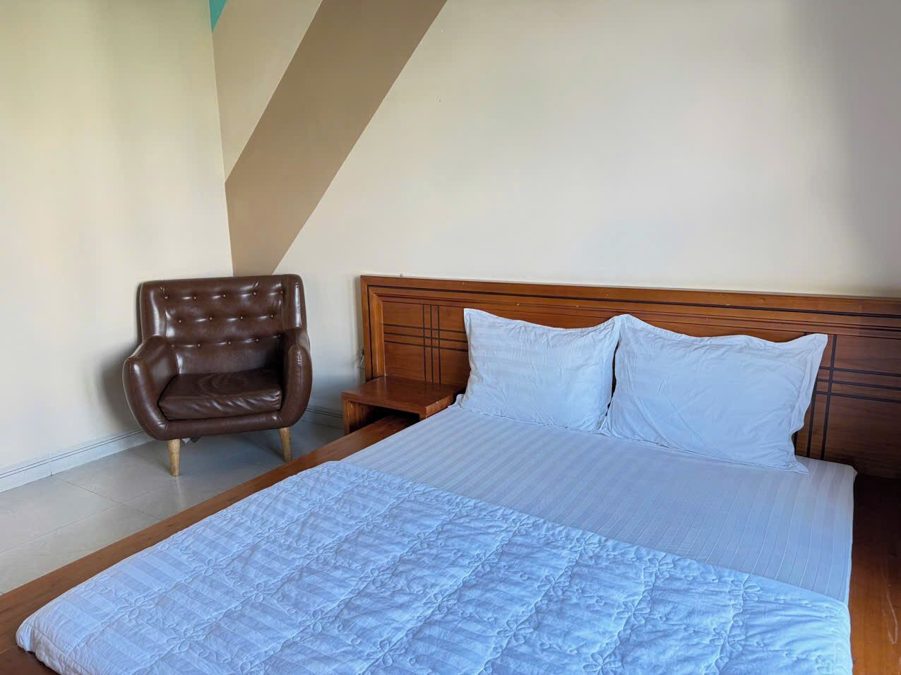Un dormitorio con una cama grande, un cabecero de madera, un sillón de cuero marrón y una pared blanca.