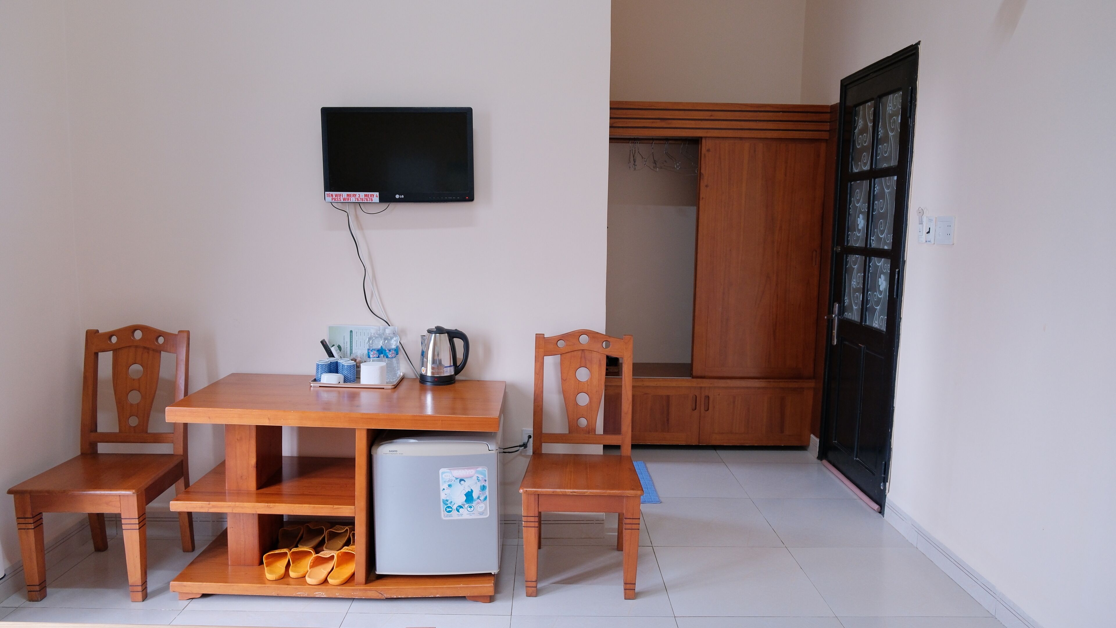 Un pequeño comedor con una mesa, sillas, un refrigerador y un televisor montado en la pared.
