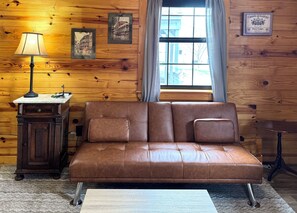 A brown leather sofa, a wooden side table with a lamp, and a framed picture on the wall.