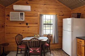 A wooden cabin interior with a dining table, chairs, a refrigerator, and an air conditioning unit.