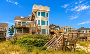 Una propiedad frente a la playa con varias casas, senderos de madera y un cielo azul despejado.