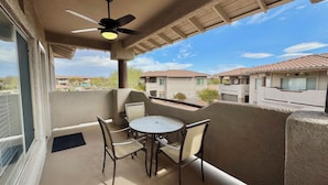 Un balcon avec une table et des chaises, un ventilateur de plafond et une vue sur les maisons voisines.