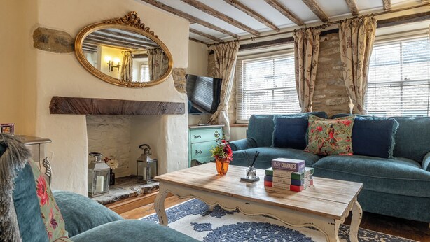 Een gezellige woonkamer met een blauwe bank, een houten salontafel met boeken, een open haard en een televisie.