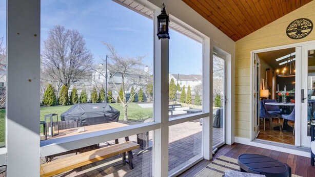 Eine überdachte Terrasse mit einem Holztisch, einer Bank und Blick auf einen Hinterhof mit einem Grill.