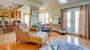 Ein geräumiges Wohnzimmer mit hohen Decken, einer Küche im Hintergrund und einer gemütlichen Sitzecke mit Sofa und Hocker.