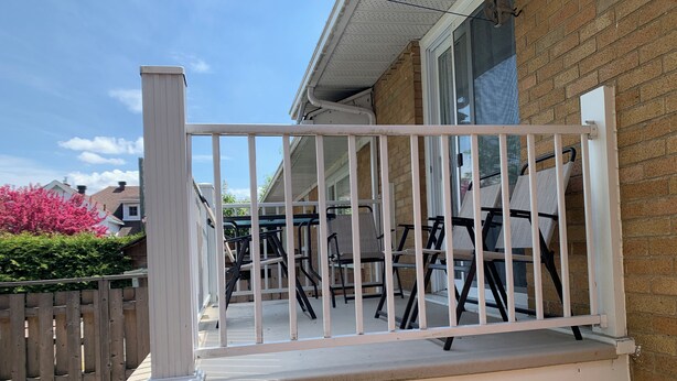 A balcony with a white railing, a wooden fence, and a brick wall.