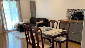 A dining area with a wooden table and chairs, a sofa, and a kitchen area with a coffee machine.
