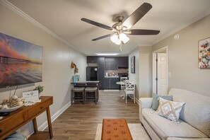 Un salon moderne avec un ventilateur de plafond, un coin repas et une cuisine en arrière-plan.