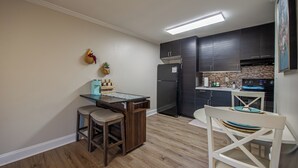 A compact kitchen with dark cabinets, a refrigerator, a microwave, and a small dining area with stools and a table. - Tallahassee Gem-Next to Doak and CollegeTown-Ideal for FSU weekend.3 minute walk (Tallahassee)
