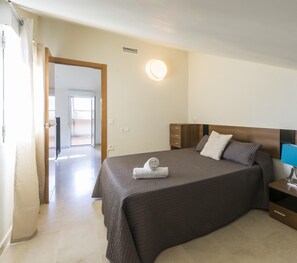 Quarto de hotel com cama, mesa de cabeceira e vista para o corredor.