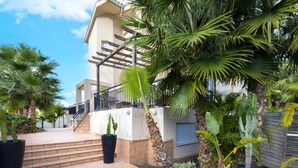 A building with a staircase leading to a balcony, surrounded by potted plants and palm trees. - COLL GROC - Nice villa with shared swimming pool in Grau i Platja (Gandia)