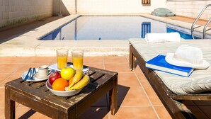 A poolside setting with a table holding fruits, a book, and a hat. - COLL GROC - Nice villa with shared swimming pool in Grau i Platja (Gandia)
