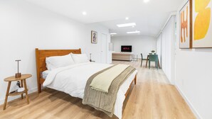 Habitació d'hotel moderna amb un llit de fusta, una taula rodona petita, un televisor i una zona de menjador amb taula i cadires.