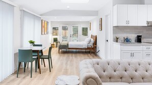 Un apartament modern amb zona de menjador, un dormitori amb llit gran, saló amb sofà i cuina amb armaris blancs.