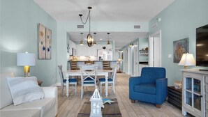 A living room with a sofa, a blue armchair, a dining table with chairs, a chandelier, and a television.