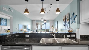 A modern kitchen with a black granite countertop, stainless steel sink, and pendant lighting.