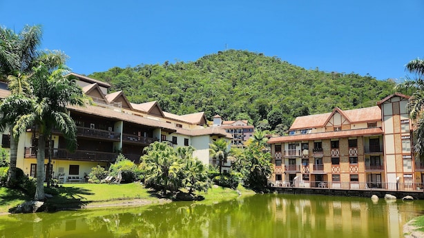 Un resort con edifici a più piani, un cortile centrale e un lago che riflette il paesaggio circostante.