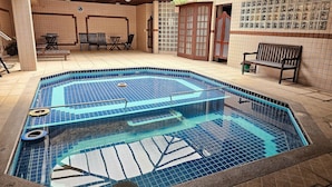Una piscina con bordo piastrellato, una panca e una porta con pannelli di vetro.