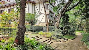 Un sentiero di giardino conduce a un edificio con architettura tradizionale, circondato da una vegetazione rigogliosa e palme.