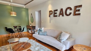 Un soggiorno con un divano, due tavolini rotondi in legno, un tavolino da caffè e un cartello appeso al muro con la scritta 'PEACE'.