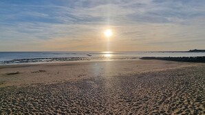 Une plage où le soleil se couche à l’horizon, avec une mer calme et des formations rocheuses visibles au loin.
