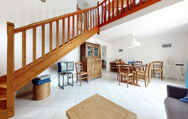 A spacious living area with a wooden staircase, a dining table with chairs, a television, and a cabinet. - Amazing home in Saint-Trojan-les-Bains with WiFi (Saint-Trojan-les-Bains)