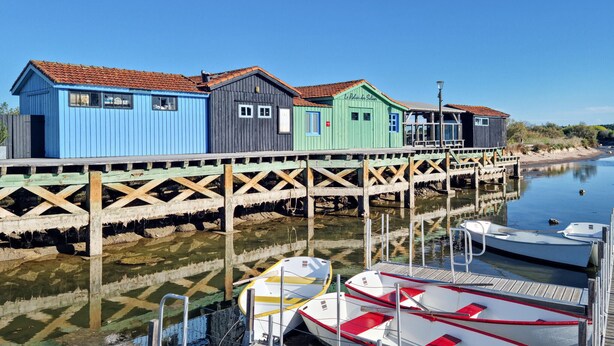 Une jetée en bois, bordée de bâtiments en bois aux couleurs vives et où sont amarrés des bateaux à son extrémité.