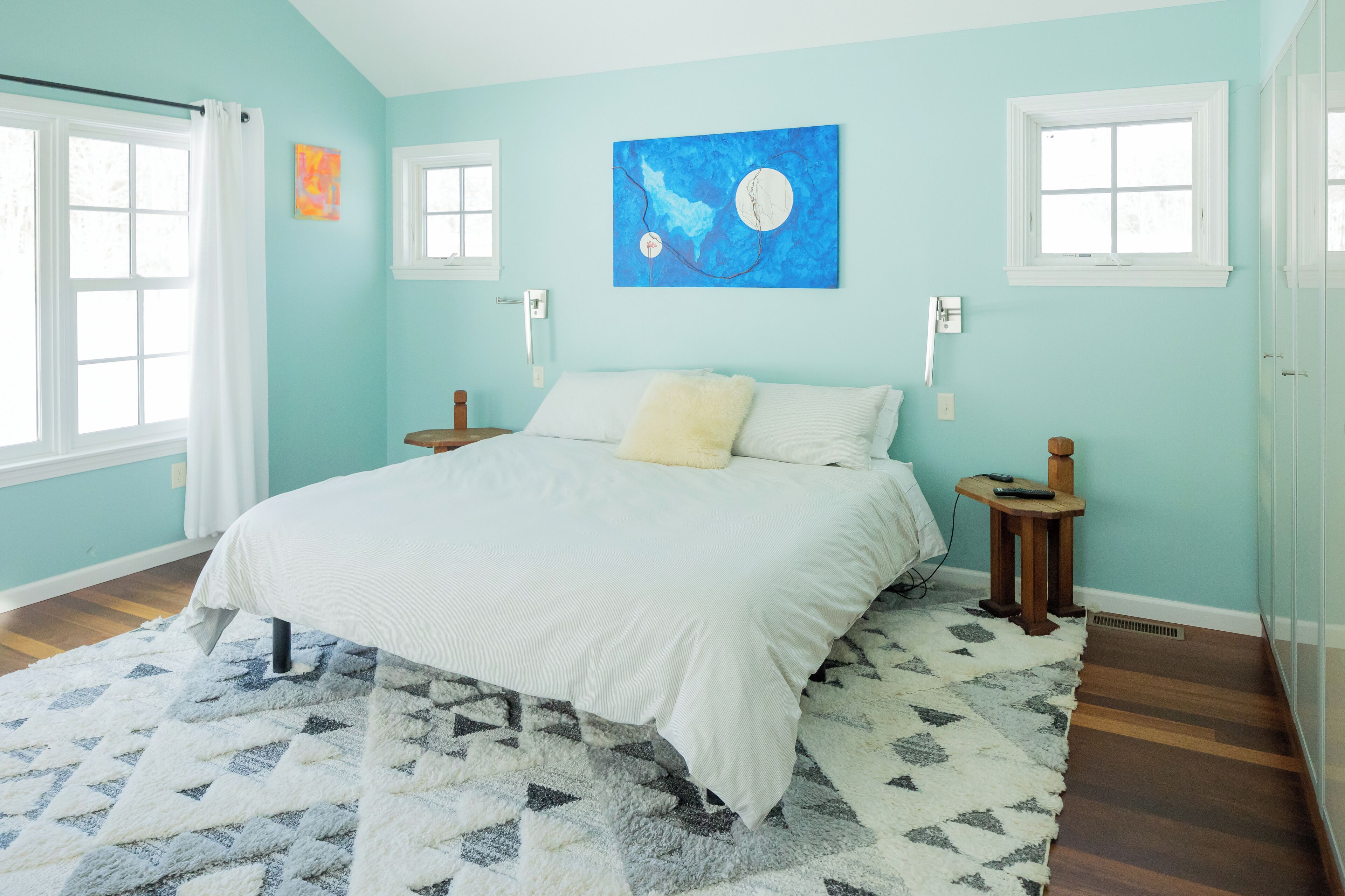 Ein Schlafzimmer mit einem großen Bett, einem Teppich mit geometrischem Muster und einem blauen abstrakten Gemälde an der Wand.
