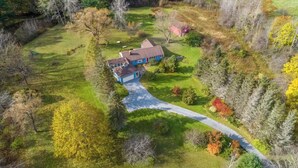 An aerial view of a house surrounded by a forested area with a driveway leading to the entrance.
