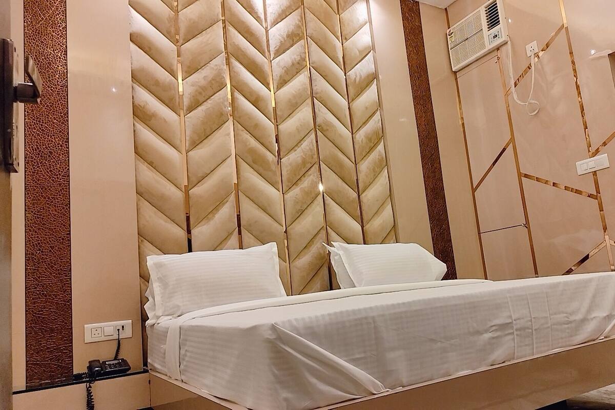 Uma cama com cabeceira em padrão losango, um telefone ao lado e uma tomada na parede.