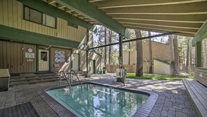 Ein überdachter Pool im Freien mit Pflasterterrasse, Holzstufen und einem Holzgebäude im Hintergrund.