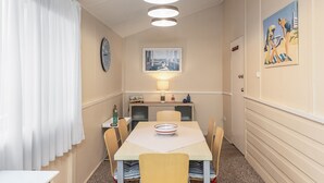 A compact dining area with a table, chairs, a clock, a lamp, and a painting on the wall. - Escape from it all at Crooked Cottage, your peaceful retreat nestled in the heart of Nambucca Heads. (Nambucca Heads)
