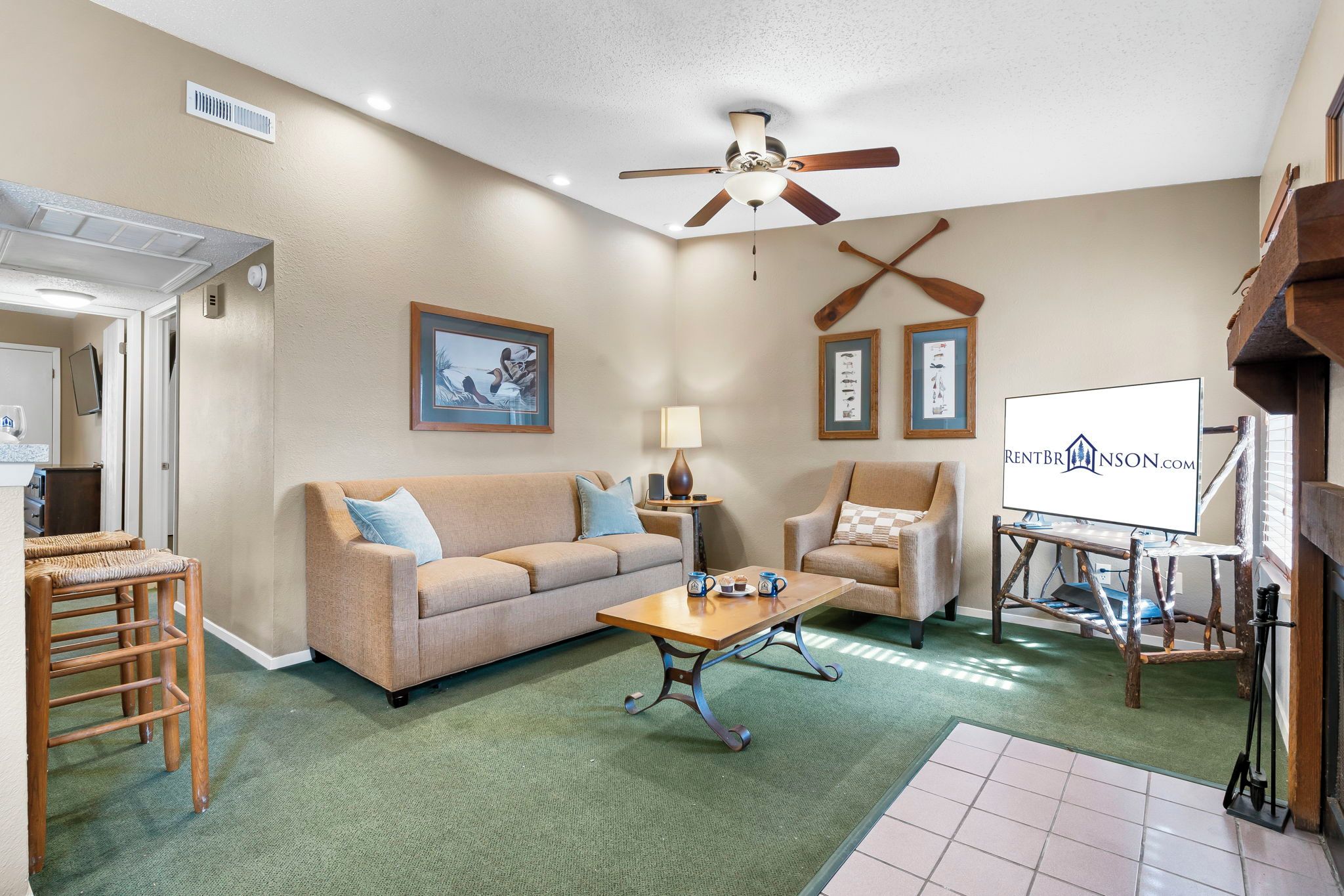 A living room with a sofa, armchairs, a coffee table, a ceiling fan, and framed pictures on the wall.