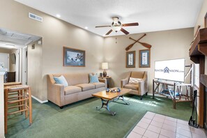 A living room with a sofa, armchairs, a coffee table, a ceiling fan, and framed pictures on the wall.