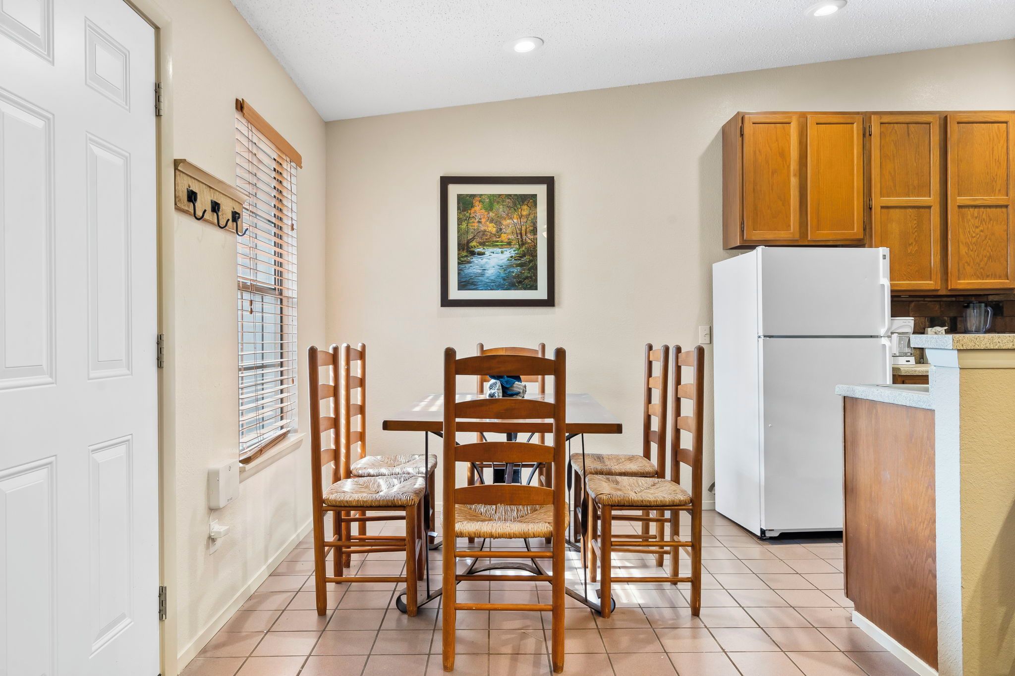 A compact kitchen with wooden cabinets, a white refrigerator, and a dining table with wicker chairs.