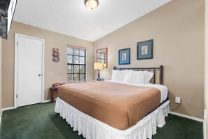 A hotel room with a large bed, a window with blinds, a bedside table with a lamp, and a door.