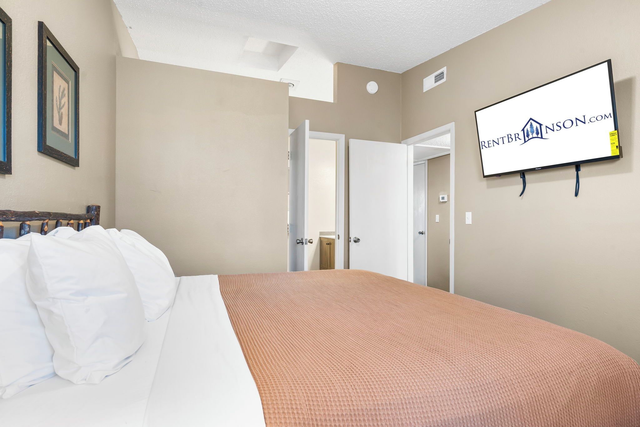 A hotel room with a bed, a television mounted on the wall, and a door leading to another room.