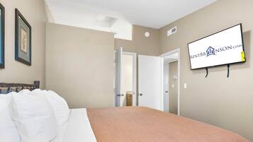 A hotel room with a bed, a television mounted on the wall, and a door leading to another room.
