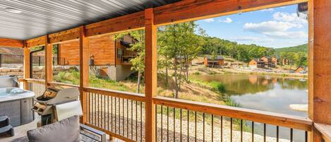 A wooden deck with a hot tub, outdoor seating, and a view of a lake and buildings.
