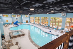Une grande piscine intérieure dotée d’un jacuzzi, de chaises longues et de grandes fenêtres.