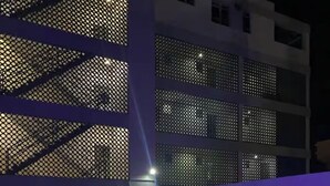 A swimming pool with a blue-lit edge, a covered outdoor seating area with chairs, and a building with a mesh facade and multiple windows. - Studio 2 minute walk to Isla Verde beach (Carolina)