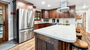 A modern kitchen with wooden cabinets, stainless steel appliances, and a large island with stools. - Charming Mountain Escape near Lake Cascade (Cascade)