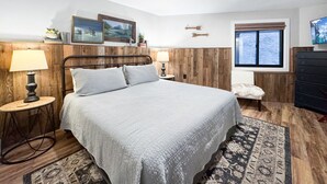 A bedroom with a large bed, a bedside table with a lamp, a chair, a dresser, and a window with a view of trees. - Charming Mountain Escape near Lake Cascade (Cascade)