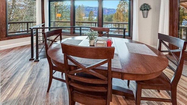 A dining area with a round table and chairs, large windows with a view of trees and mountains, and a wooden floor. - Charming Mountain Escape near Lake Cascade (Cascade)