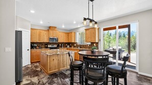 A kitchen with wooden cabinets, a central island, and a dining area with chairs. - Mountain Retreat with Hot Tub & Game Room (Donnelly)