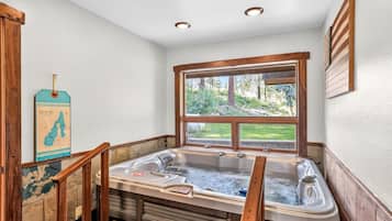 A hot tub with wooden railings, a window with a view of greenery, and a map on the wall.